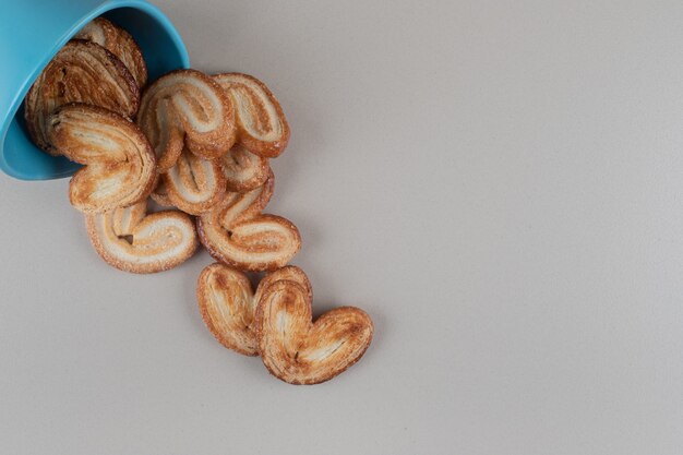 Flaky cookies spilling out of a bowl on marble background.