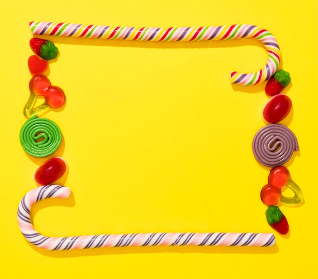 Flat lay arrangement of candies on yellow background with copy space
