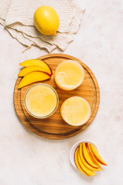 Flat lay arrangement of fresh smoothies next to sliced mango