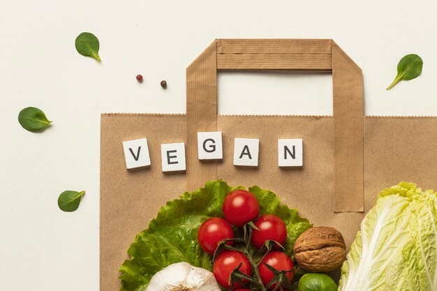 Flat lay of assortment of vegetables with paper bag and the word vegan