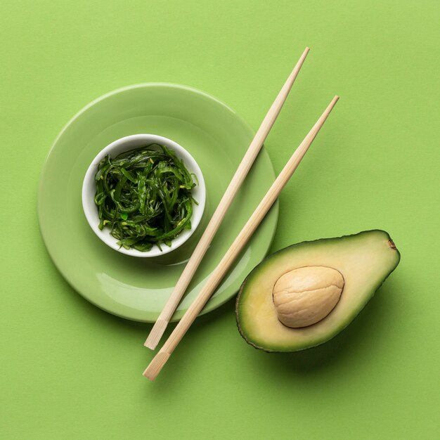 Flat lay of avocado with bowl of greens