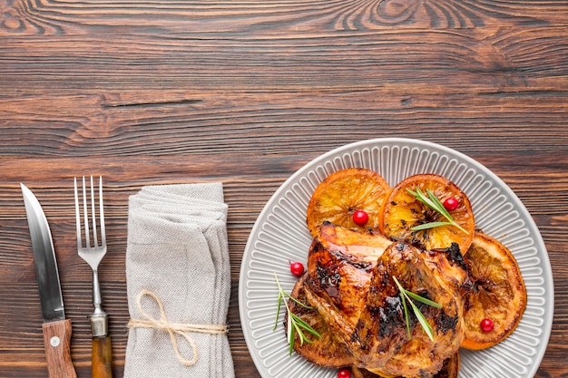 Flat lay baked chicken and orange slices on plate with cutlery and napkin