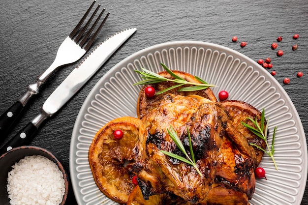 Flat lay baked chicken and orange slices on plate with cutlery