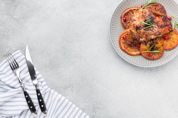 Flat lay baked chicken and orange slices on plate with kitchen towel and copy-space