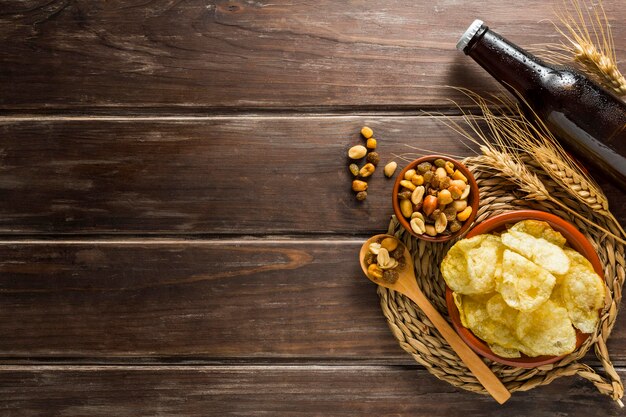 Flat lay of beer bottle with chips and nuts