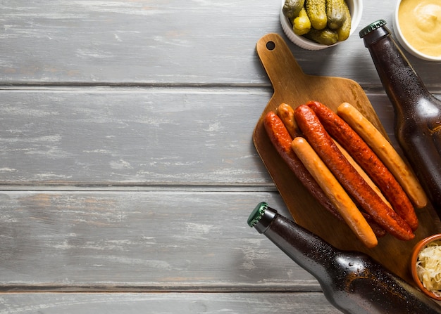 Flat lay of beer bottles with sausages and pickles