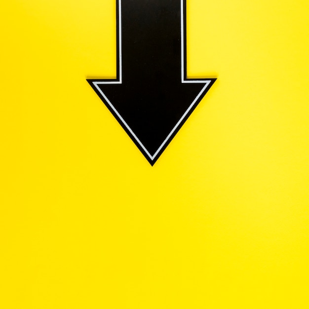 Free photo flat lay black arrow downwards on yellow background with copy-space