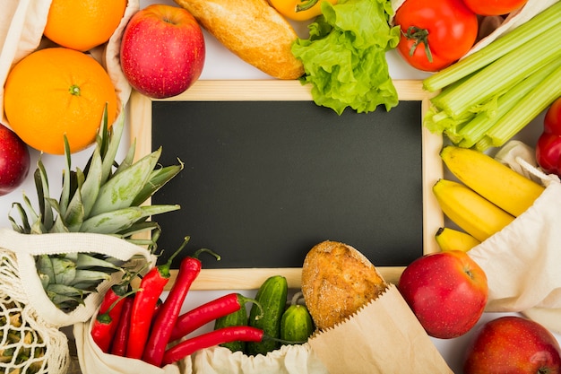 Flat lay of blackboard with fruit and vegetables in reusable bags