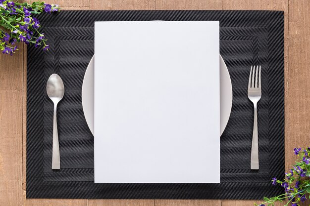 Flat lay of blank menu paper on plate with flowers and cutlery