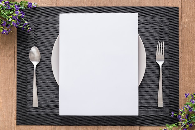 Flat lay of blank menu paper on plate with flowers and cutlery