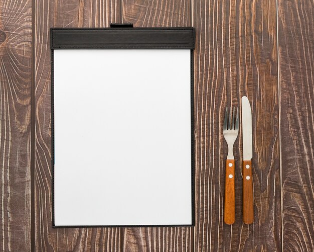 Flat lay of blank menu on wooden surface with cutlery