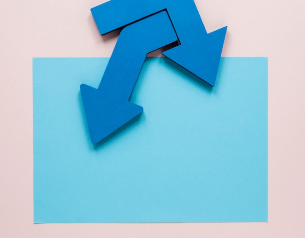 Free photo flat lay blue arrows and blue cardboard mock-up on pink background