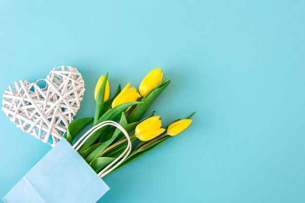 Flat lay blue background with yellow tulip flowers in a paper bag