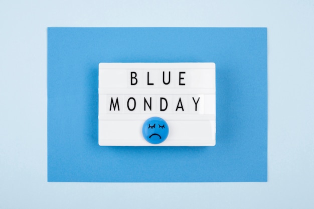 Flat lay of blue monday light box with sad face