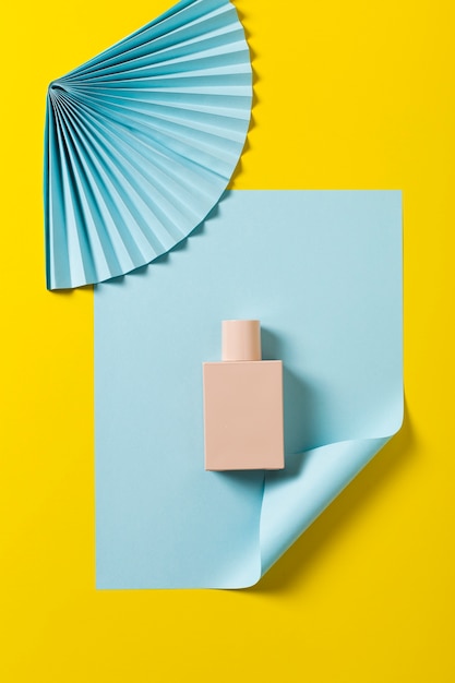 Flat lay of bottle and fan on yellow background