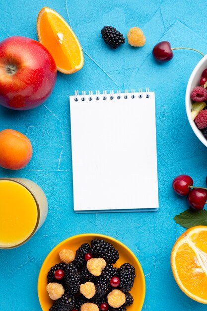 Flat-lay bowl of fresh berries and fruits with notepad