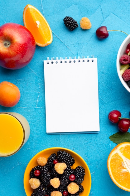 Flat-lay bowl of fresh berries and fruits with notepad