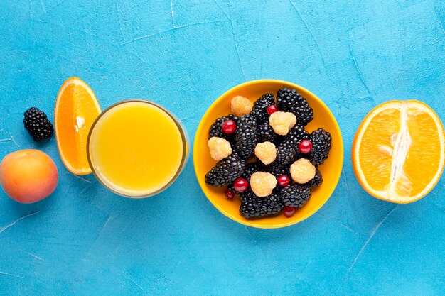 Flat-lay bowl of fresh berries with juice and oranges
