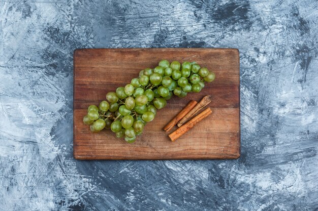 Flat lay bowl of grapes, cinnamon on cutting board on dark blue marble background. horizontal