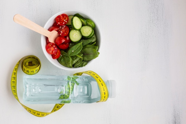 Foto gratuita piatto disteso di ciotola di insalata e bottiglia d'acqua