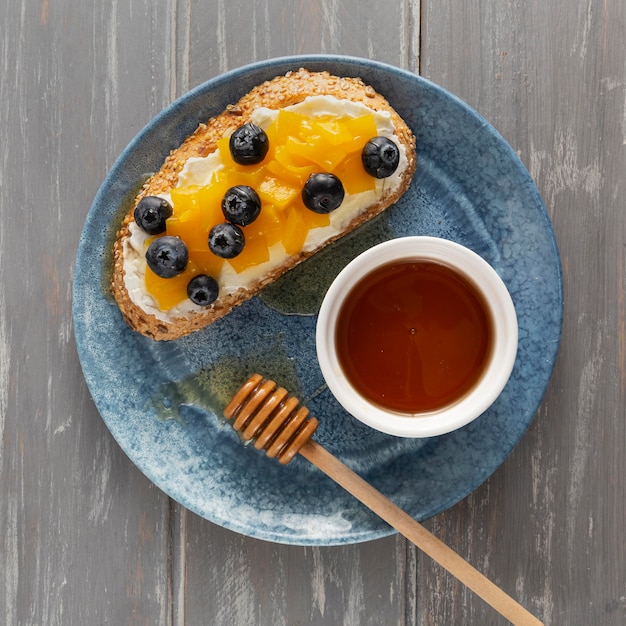 Flat lay bread with cream cheese and fruits on plate with honey