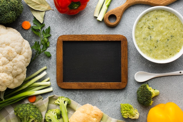 Flat lay broccoli bisque and vegetables with blank blackboard