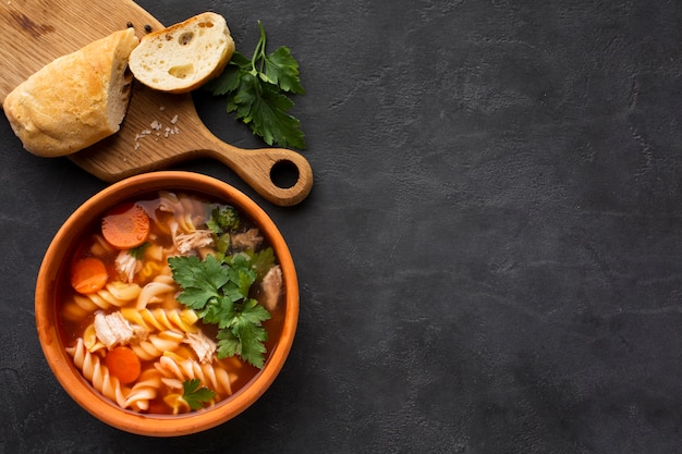 Flat lay broccoli carrots and fusilli in bowl with bread on cutting board with copy space