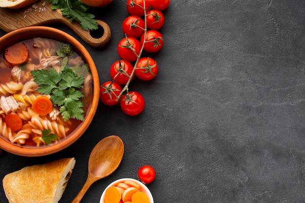 Flat lay broccoli carrots and fusilli in bowl with bread and wooden spoon with copy space