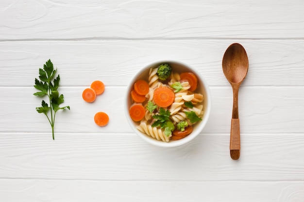 Flat lay broccoli carrots and fusilli in bowl with wooden spoon