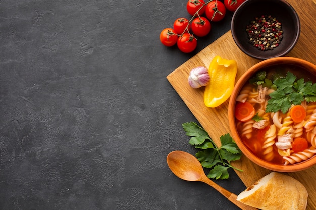 Flat lay broccoli carrots and fusilli soup in bowl with bread and wooden spoon with copy space