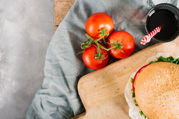 Flat-lay burger on wooden board with fresh tomatoes