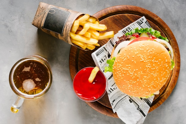 Flat-lay burger on wooden board with fries and beer