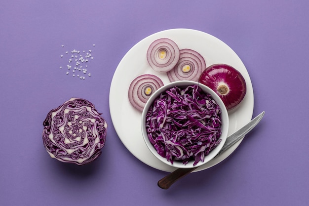 Flat lay of cabbage in bowl with onion on plate and knife