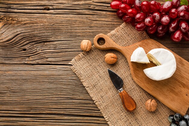 Flat lay camembert grapes and walnuts on wooden cutting board with copy space