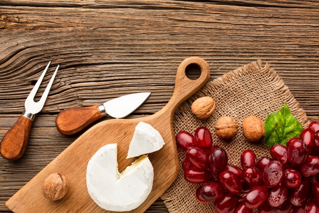 Flat lay camembert grapes and walnuts on wooden cutting board with ustensils