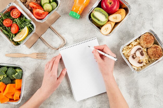 Flat lay of casseroles with meals and hand writing on notebook