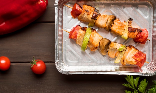 Flat lay chicken skewers on tray with red pepper and tomatoes