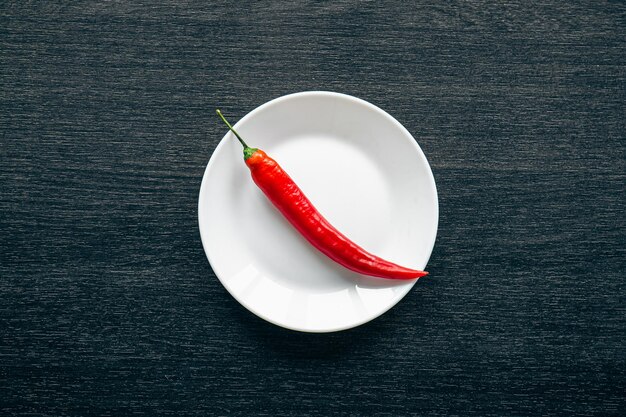 Flat lay chili peppers on a white plate on a black background