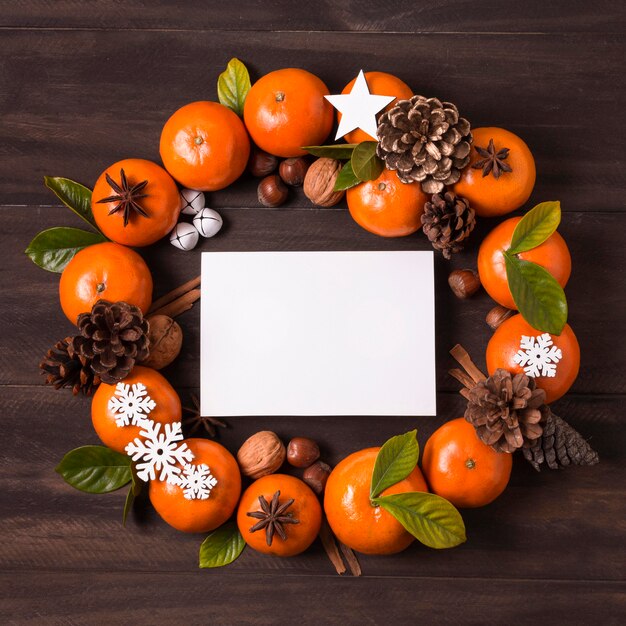 Flat lay of christmas wreath make of tangerines and pine cones with blank paper