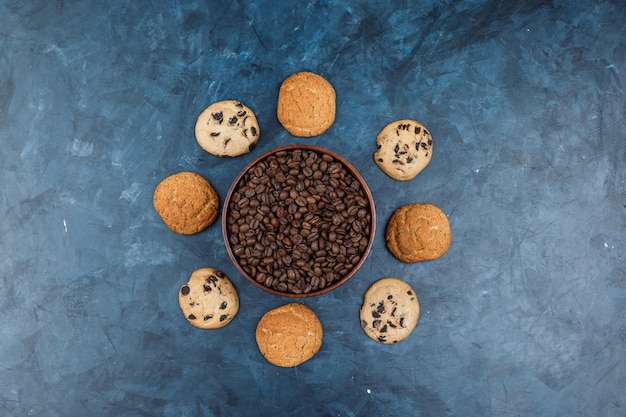 Foto gratuita chicchi di caffè piatti laici nella ciotola con diversi tipi di biscotti su sfondo blu scuro. orizzontale