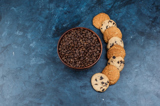 Flat lay coffee beans in bowl with different types of cookies on dark blue background. horizontal