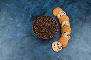 Free photo flat lay coffee beans in bowl with different types of cookies on dark blue background. horizontal