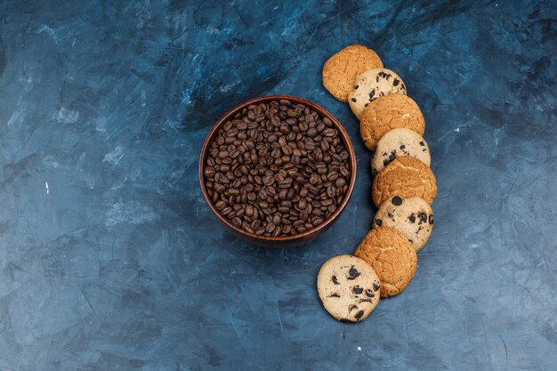 紺色の背景にさまざまな種類のクッキーとボウルに平らなコーヒー豆を置きます。水平