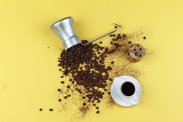 Flat lay coffee beans in jug with glass jar, cup of coffee, chocolate chip cookies on yellow background. horizontal