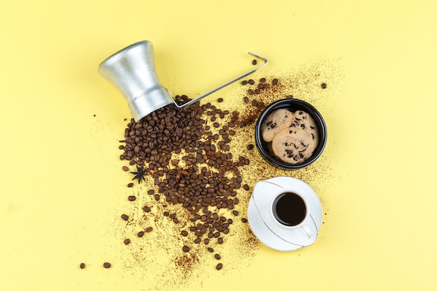 Flat lay coffee beans in jug with glass jar, cup of coffee, chocolate chip cookies on yellow background. horizontal