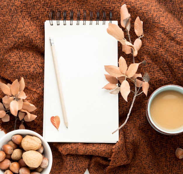 Flat lay of coffee mug with autumn leaves and notebook