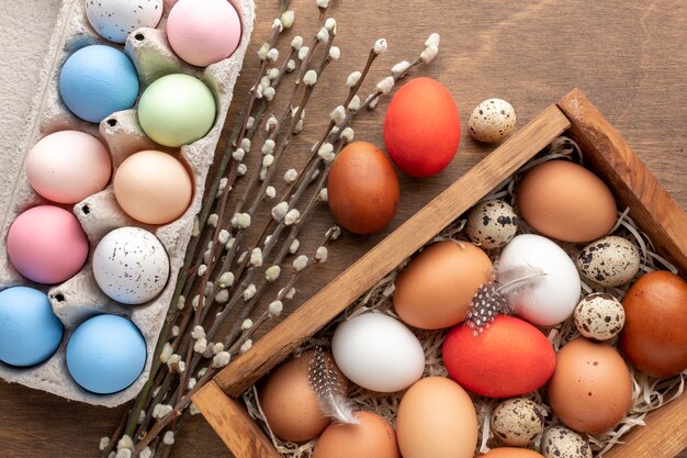 Free photo flat lay of colorful eggs for easter in box and carton with flowers
