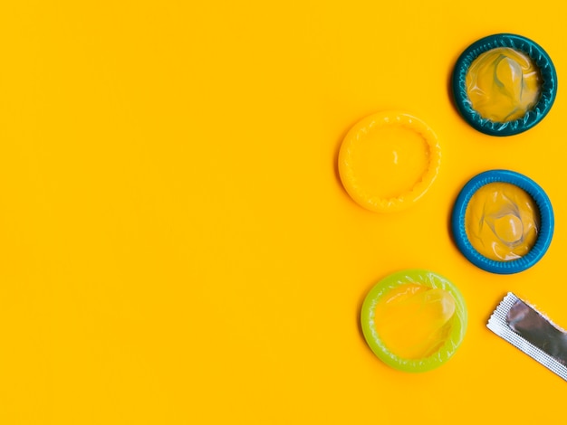 Flat lay colourful condoms on yellow background 