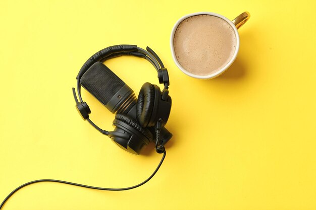 Flat lay composition with Microphone for podcasts and black studio headphones on yellow background with coffee learning online education concept
