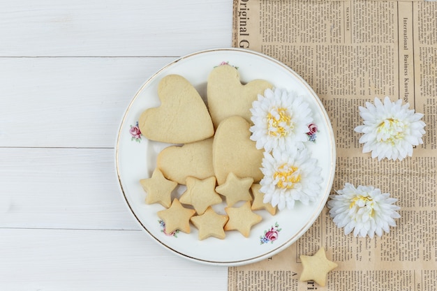 Biscotti piatti laici nel piatto con fiori su fondo in legno e giornale. orizzontale